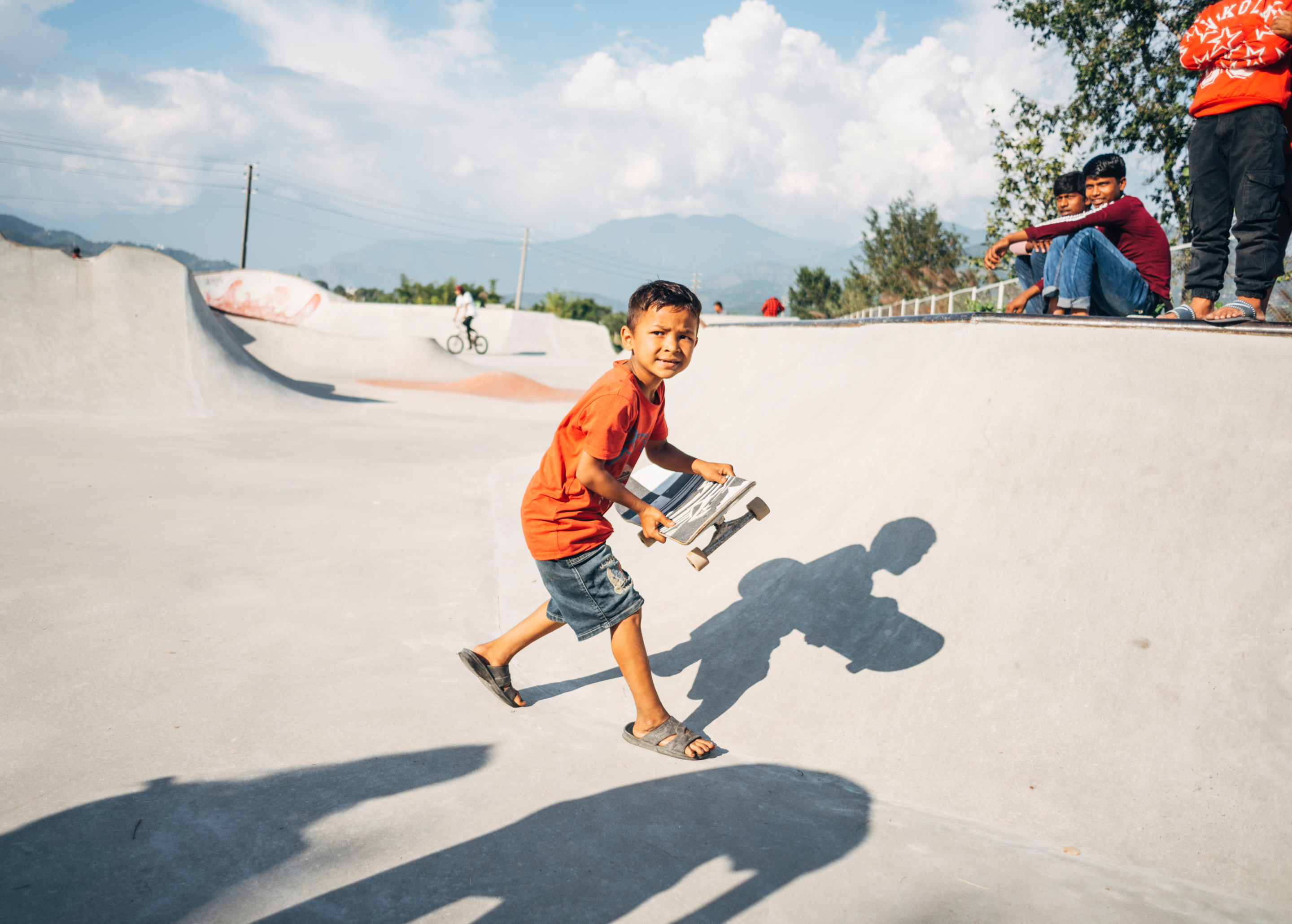 A young child holding a skateboard in a skateboard ramp.